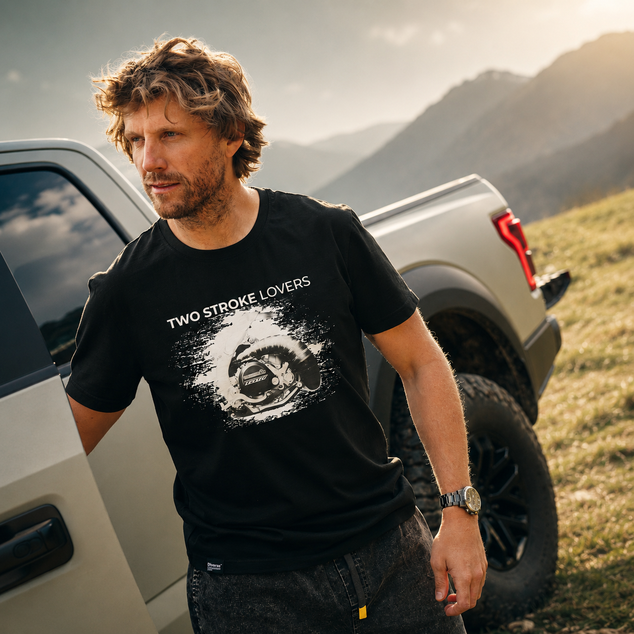 Adrien Van Beveren portant le T-shirt T500 Noir Two Stroke Lovers devant un pickup dans un paysage de montagne